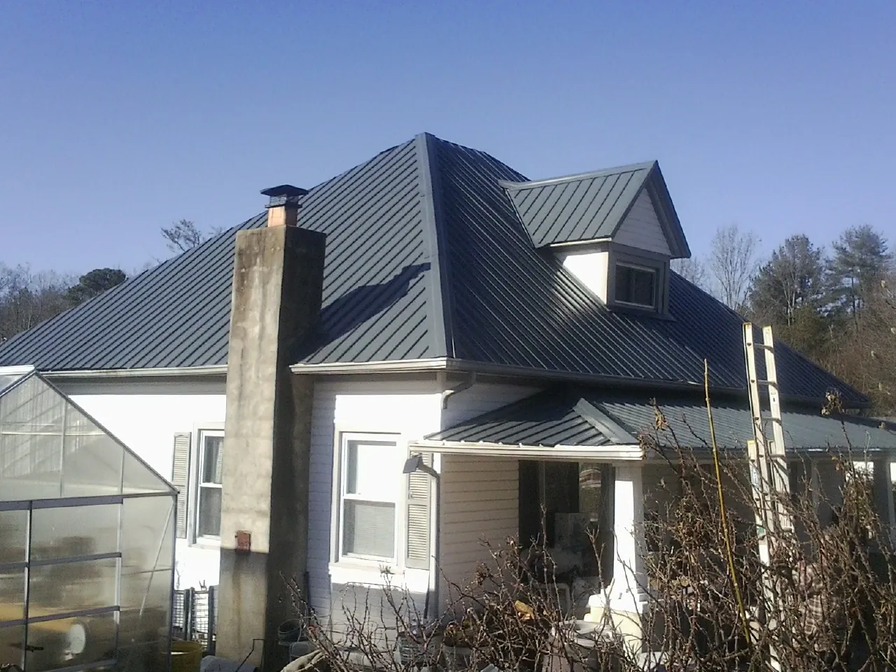 Dark blue standing seam metal roof on a white farmhouse with dormer — Slate & Tile Roof Repair by Roofing Brothers in Abbeville