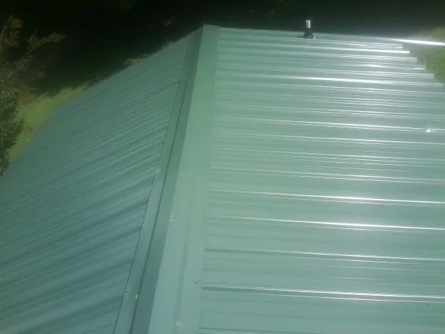 New green metal panels meeting at the ridge of a roof — Flat Roof Repair work by our crew in Abbeville